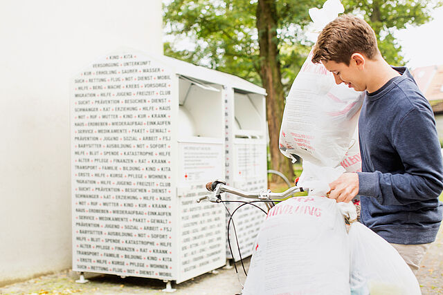 Frau spendet Klamotten an DRK-Kleidercontainer